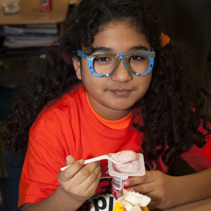 Latino girl eating yogurt and smiling